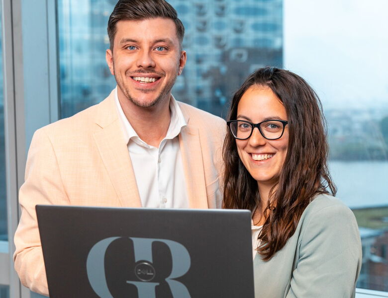 Zwei Teammitglieder von Grabowski & Rohmann Personalberatung Hamburg – Mann im beigefarbenen Sakko und Frau im mintfarbenen Blazer arbeiten gemeinsam am Laptop im Büro mit Elbblick