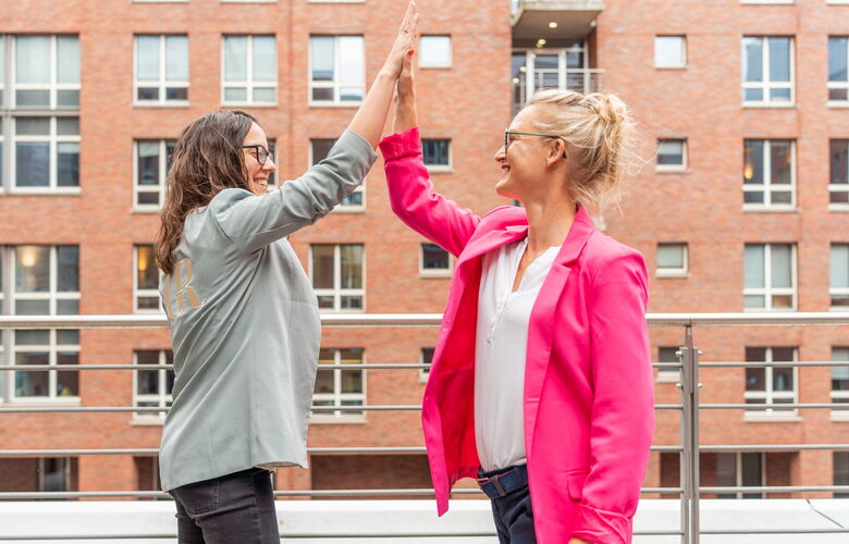 Zwei Personalberaterinnen geben sich ein High Five auf einer Dachterrasse für erfolgreiche Zusammenarbeit bei Grabowski & Rohmann Personalberatung Hamburg